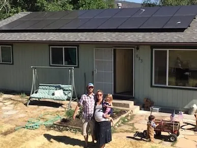 Man, Woman and baby standing in front of a house with solar panels installed