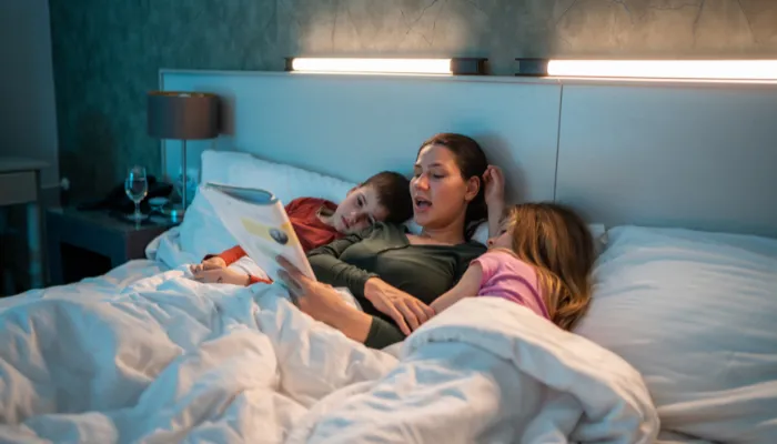 A mom reading to her kids in bed.