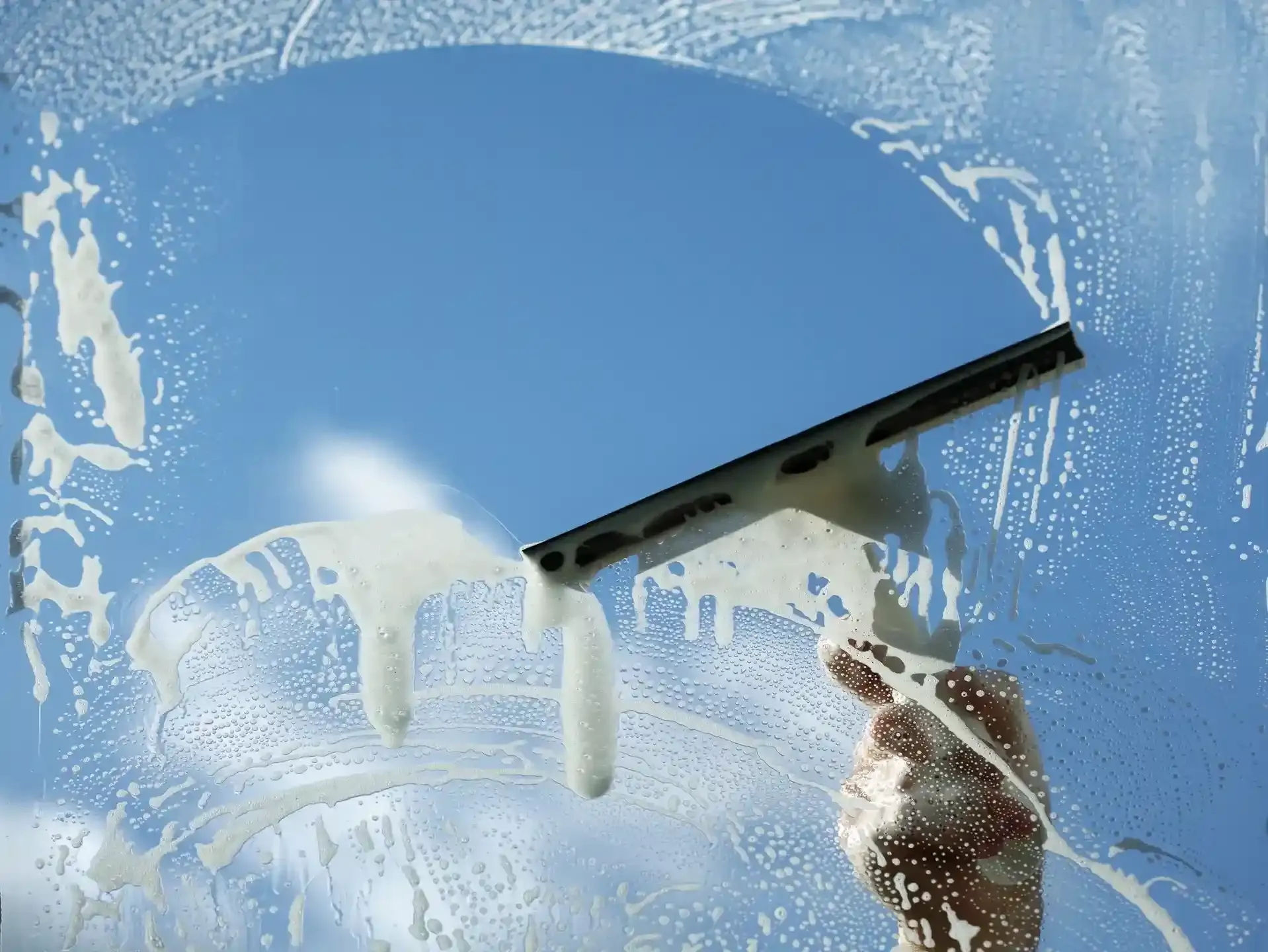 Hand using squeegee to clean soapy glass window leaving clear streak-free surface