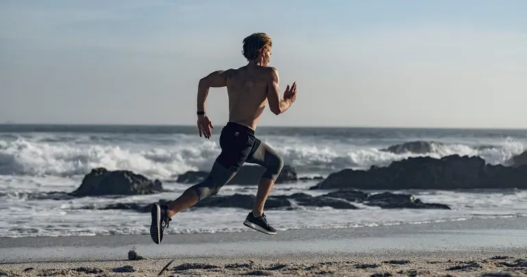 A man with no shirt on sprinting on a beach.