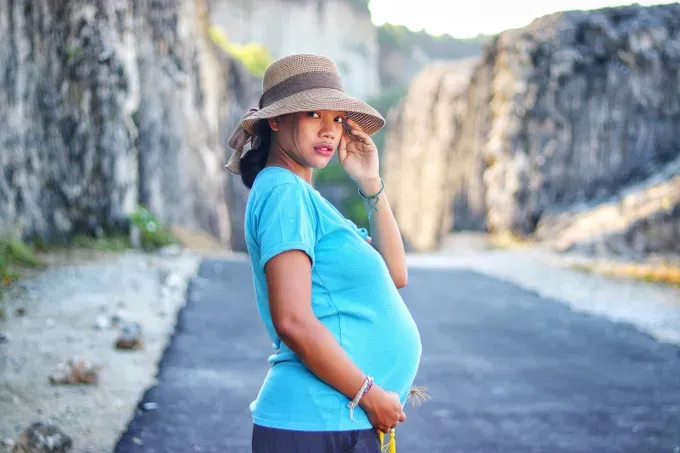 Pregnant woman in a comfortable dress, gently resting her hands on her rounded belly, smiling softly