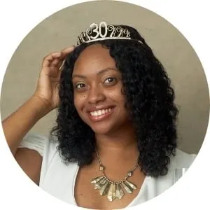 Dark skinned woman wearing a tiara posed in front of a taupe backdrop for a portrait