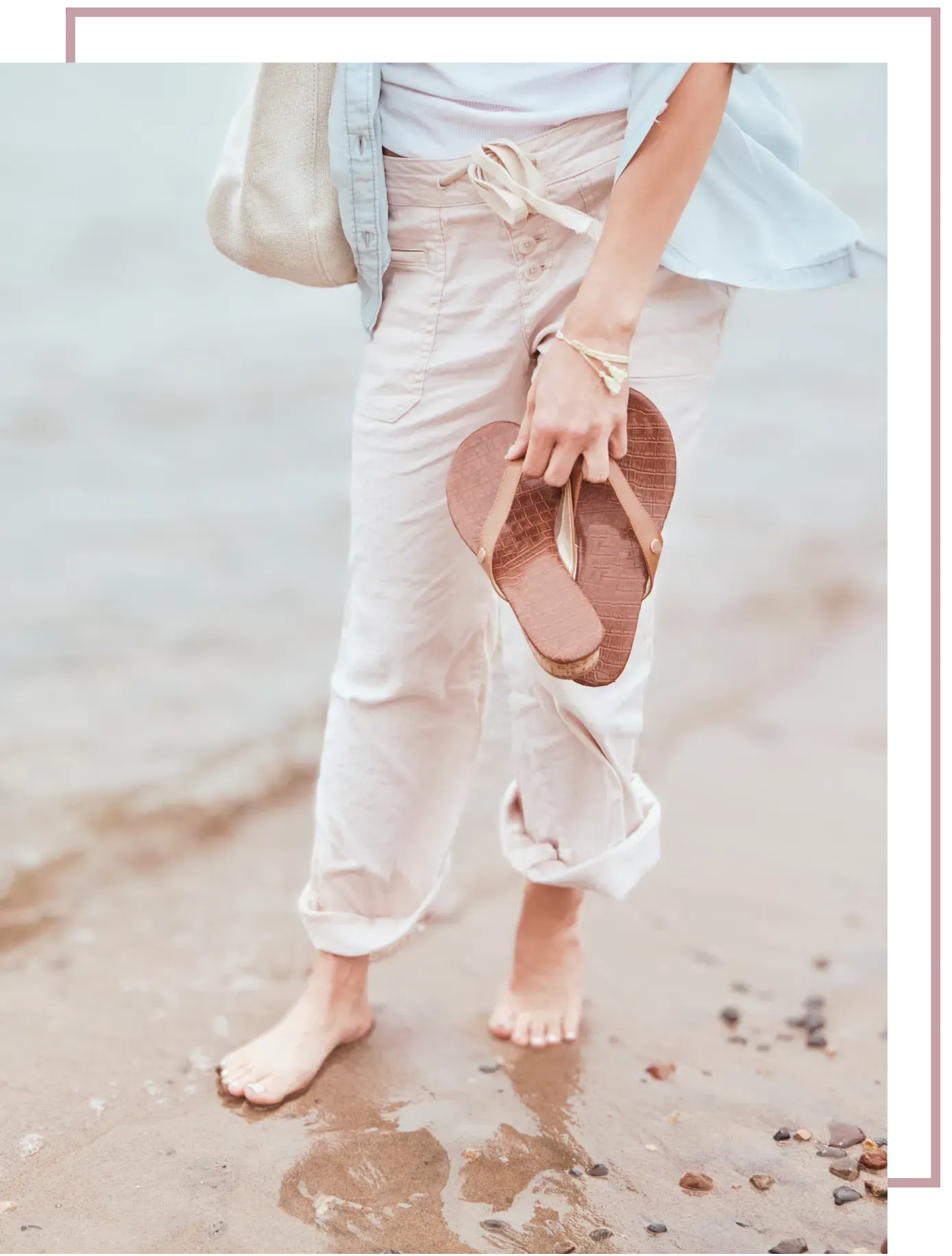 a woman walking on beach holding her shoes