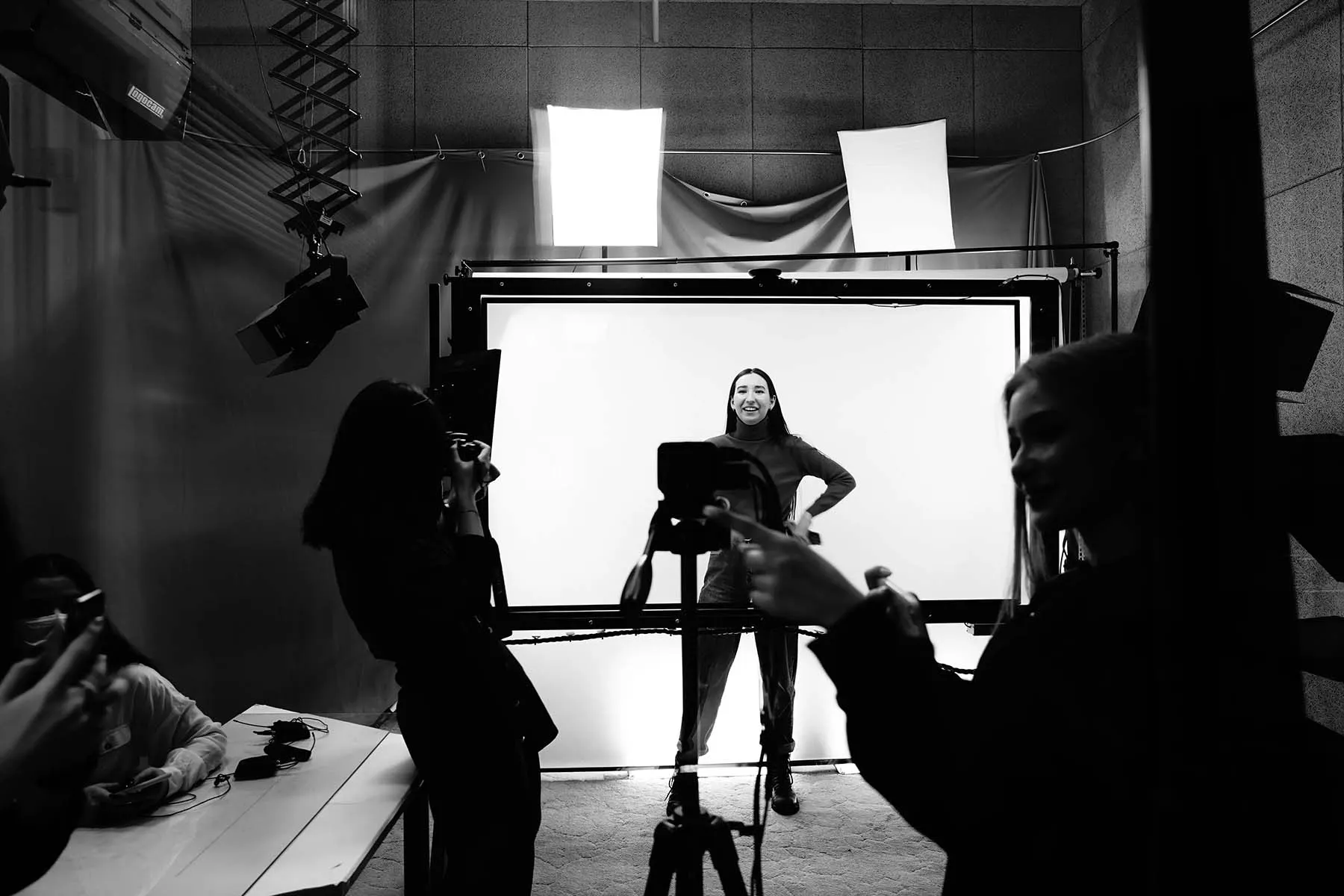 Black and white image of a photography studio with a client posed in front of a white backdrop