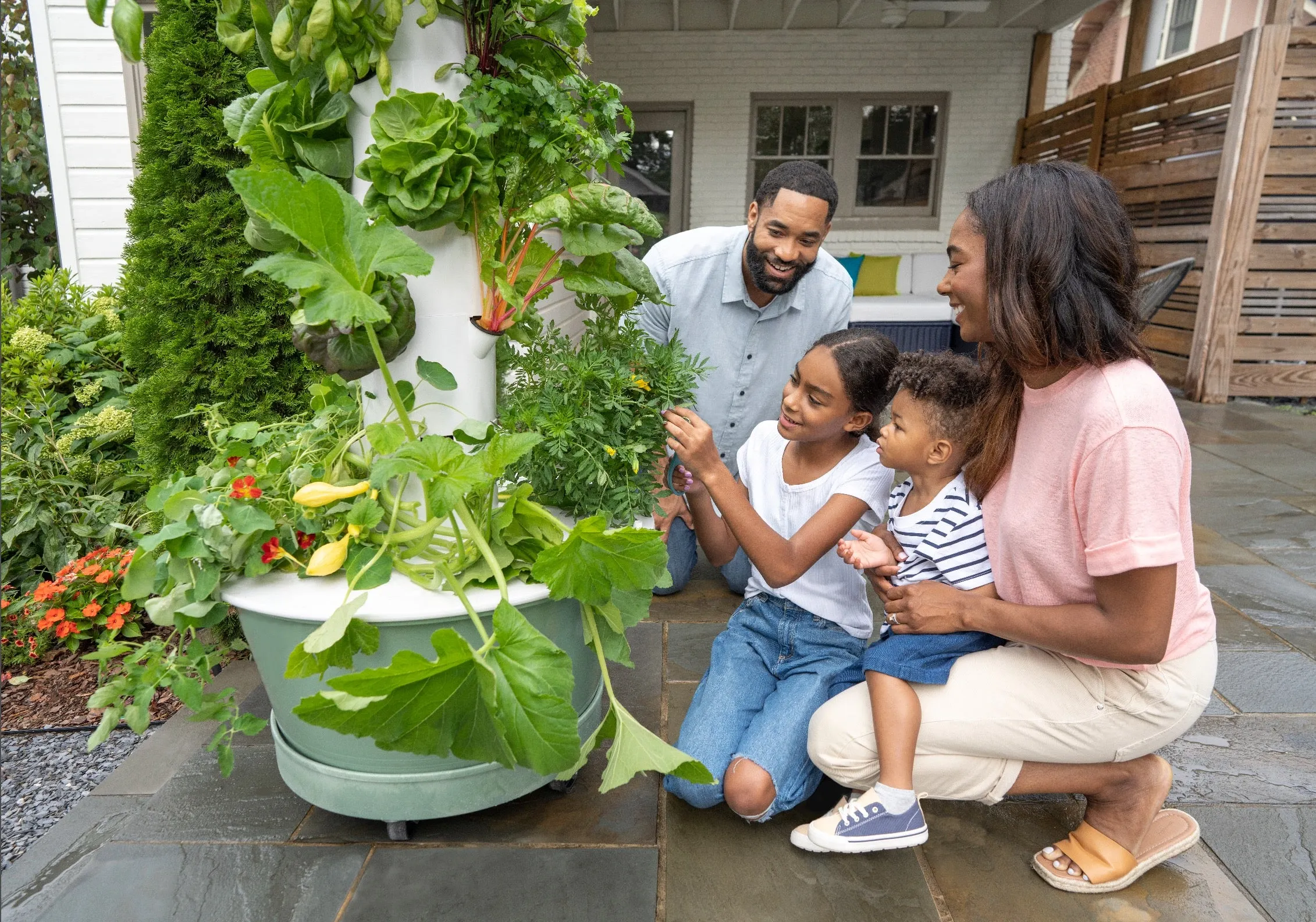 Family harvesting Tower Garden-grown leafy greens, tomatoes, and herbs for Nutritarian-inspired salad.