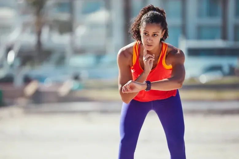 A woman in running clothes checking neck pulse while looking at her smartwatch.