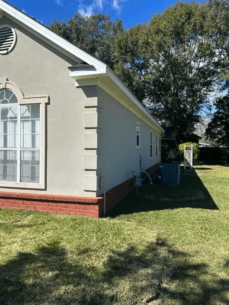 <alt=“After stucco house soft wash in Dawes, Mobile County, Alabama showing clean exterior walls bright trim and restored brick foundation.”>