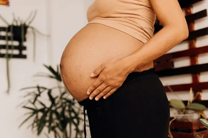 Expecting mother gently holding her rounded belly, looking content and serene.