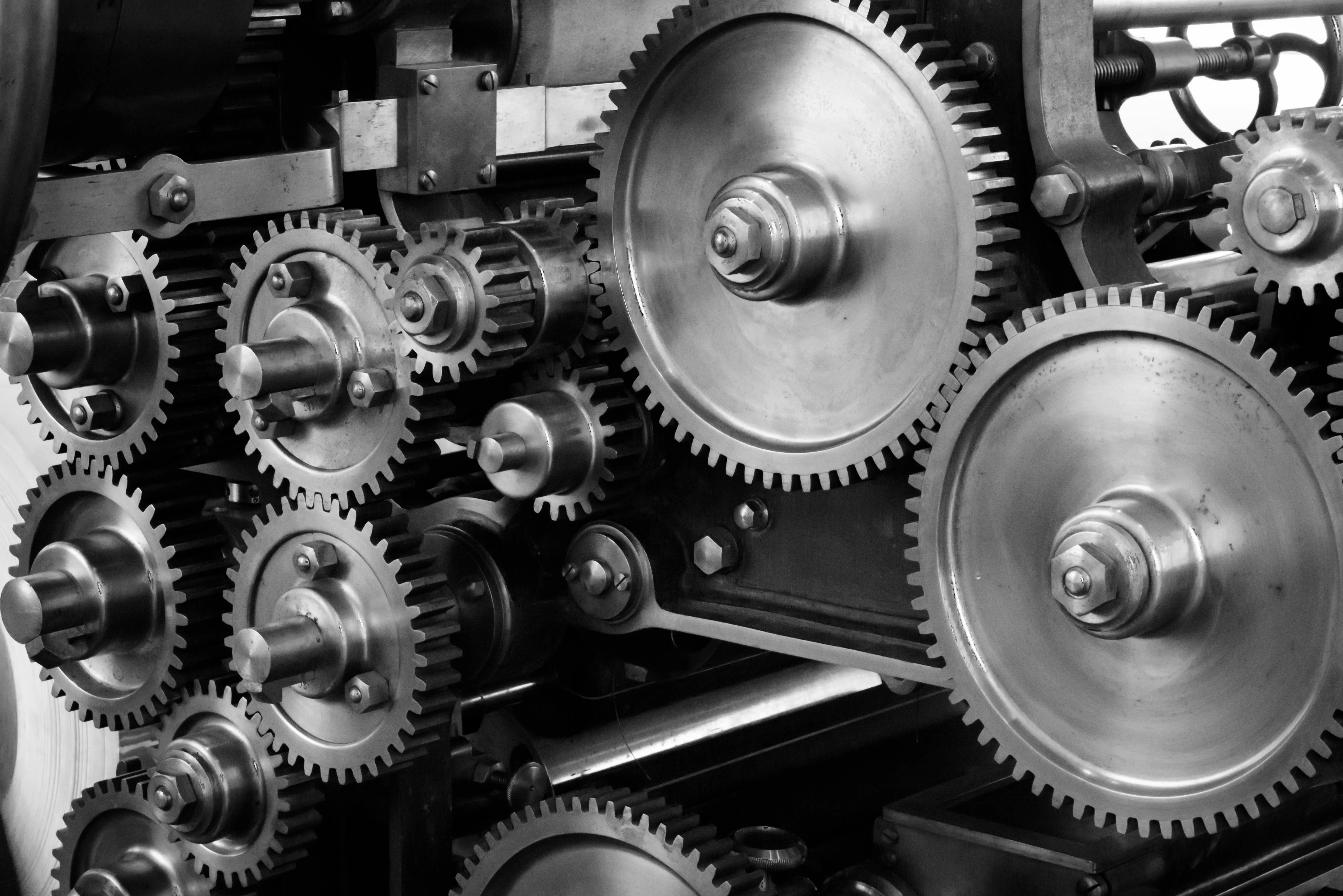 Black-and-white image of interlocking metal gears forming a mechanical system. Symbolizes the UHI Flywheel—how digital assets compound through creation, distribution, monetization, authority, and repetition to generate unstoppable income momentum.