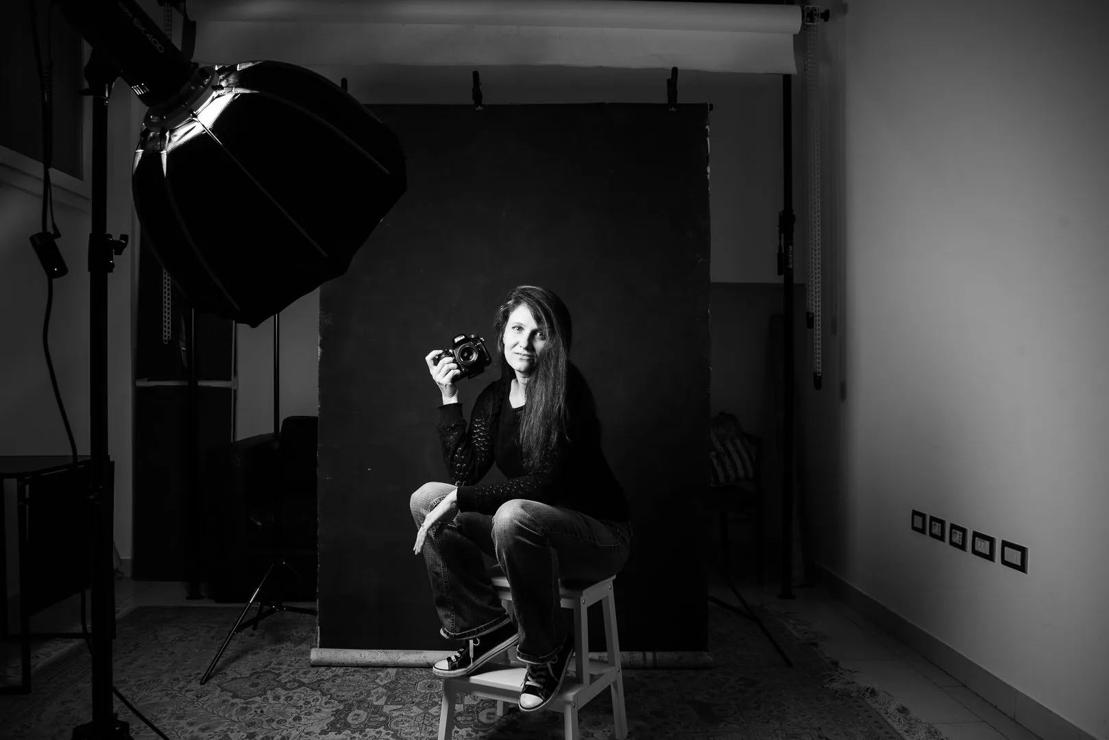 ritratto in bianco e nero di fotografa di ritratto con macchina fotografica in mano, luce flash a destra della persona, studio fotografico con sfondo 