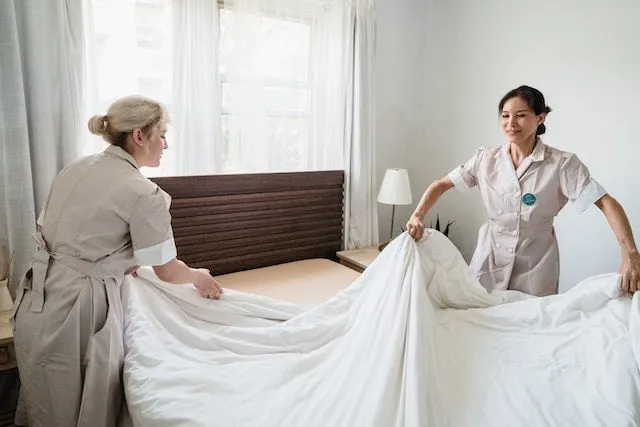 Two female caregivers changing the sheets on a bed