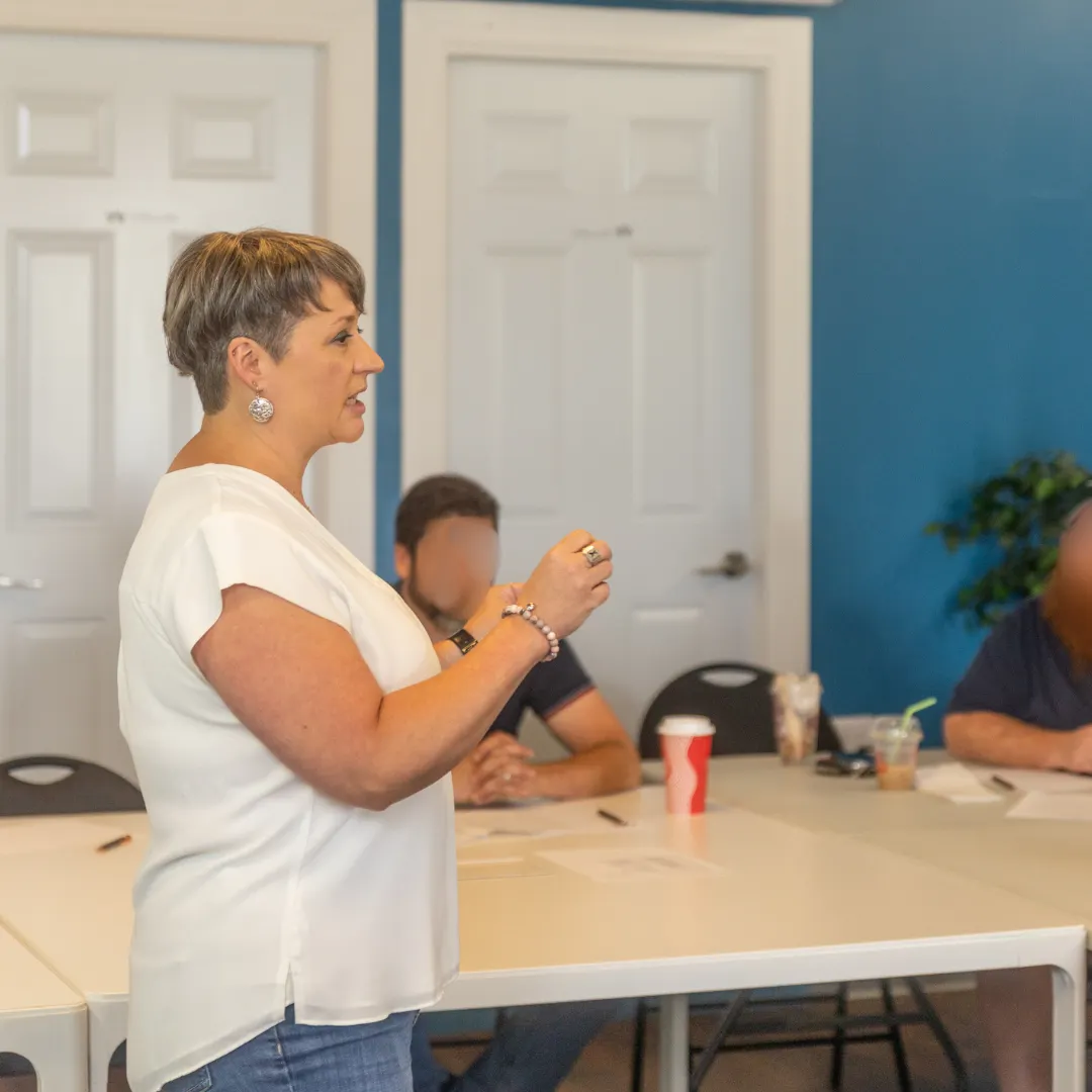 A woman standing at the front of a room presenting to folks sitting down. 
