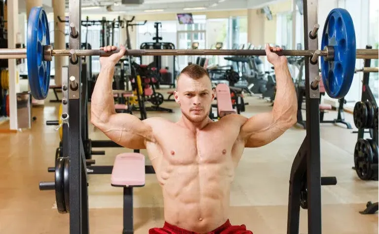 Man in gym with no shirt on doing an overhead press.