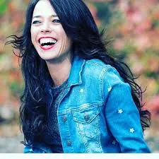 Kristin smiling huge with long black hair and a blue denim jacket