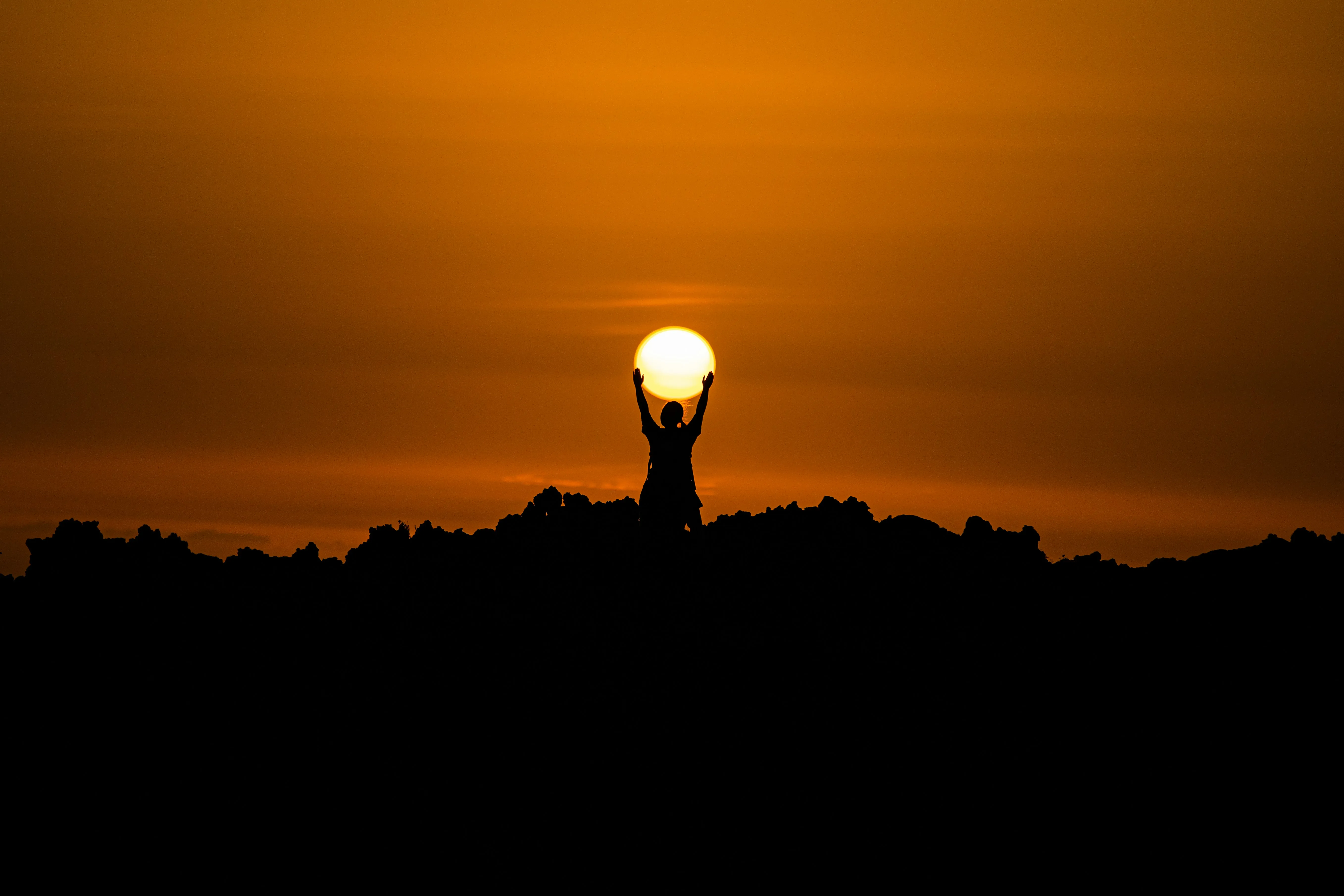 sillohouette of a man holding the sun at sunset