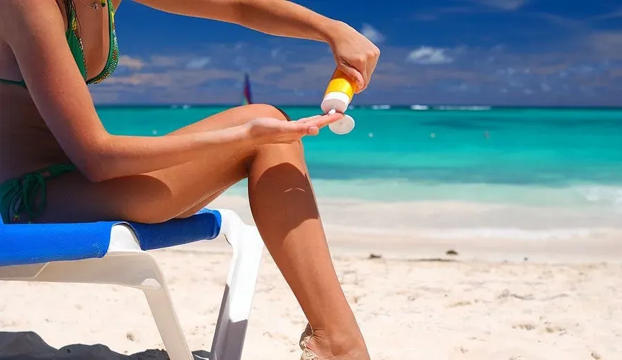 A woman applying sunscreen to her legs sitting on a beach.